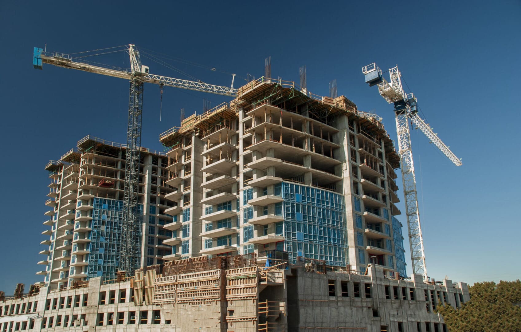 White crane towers at a large construction site with condominium balconies against a blue sky